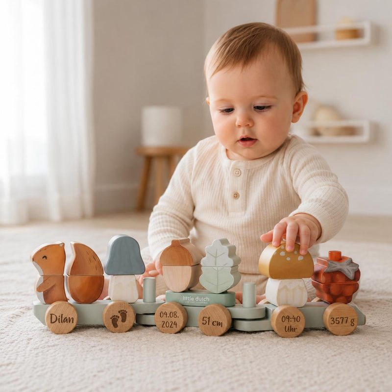 Baby spielt mit personalisiertem Holzzug zur Geburt mit Name, Wunschdatum, Uhrzeit, Größe und Gewicht im Babyzimmer