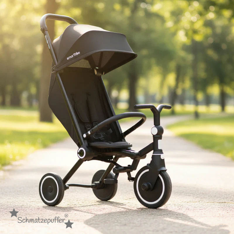 Schwarzes smarTrike Dreirad mit Kinderwagenfunktion im Park mit Schmatzepuffer Logo im Lifestyle-Bild